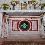 Al centro il grazioso altare in legno, ricco di immaginette sacre e vasetti di fiori, mostra nella base eleganti elementi ricolorati nel tempo con toni rosso, verde e dorato coperti da una bianca tovaglia ricamata